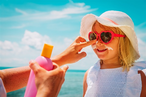 Young girl with hat and sunglasses putting sunscreen on nose