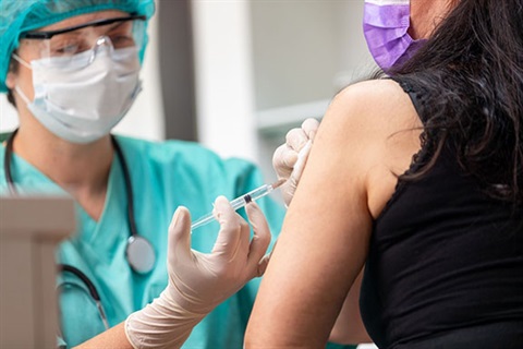 Nurse in full PPE administers a flu shot to a patient who is wearing a mask.