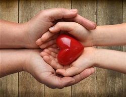 Adult hands holding child's hands holding a heart