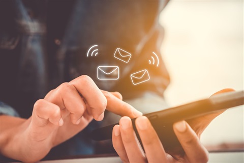 Person using a smartphone with animated email icons floating above the screen, symbolizing sending or receiving messages.