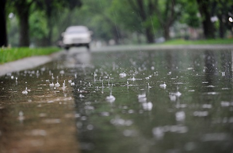 Rain water falling in the street in front of a car.