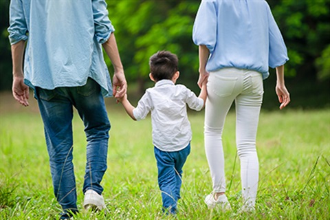 Man and woman holding hands with a child while walking in a park