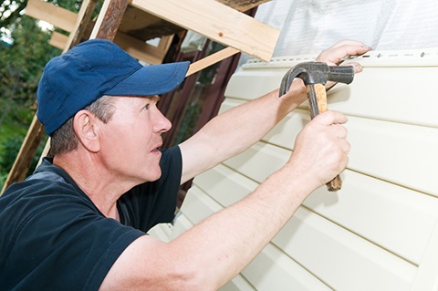 Person hammering a nail into the siding of a house