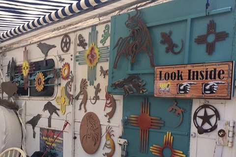 Wall decorated with metal art including lizards, sunflowers, stars, and a 'Look Inside' wooden sign with pointing hands.