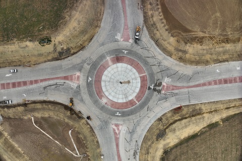 An aerial view of a roundabout being constructed. Vehicles sit in the lanes. 